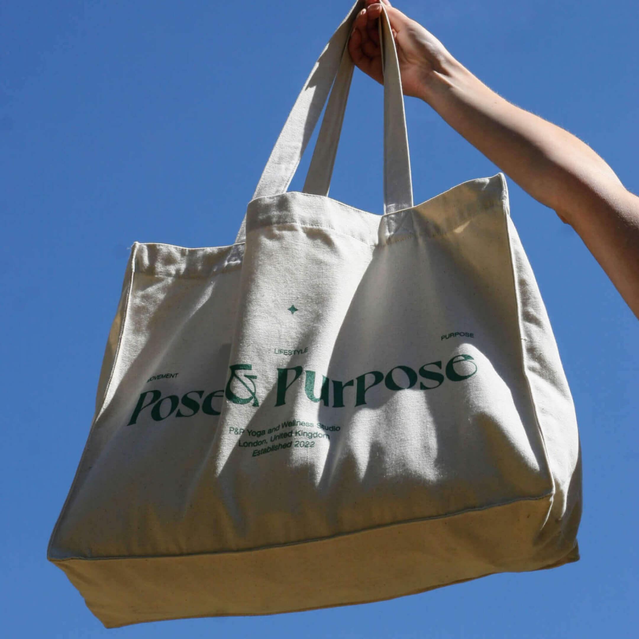 Photo of Pose & Purpose tote bag held behind against green hedge